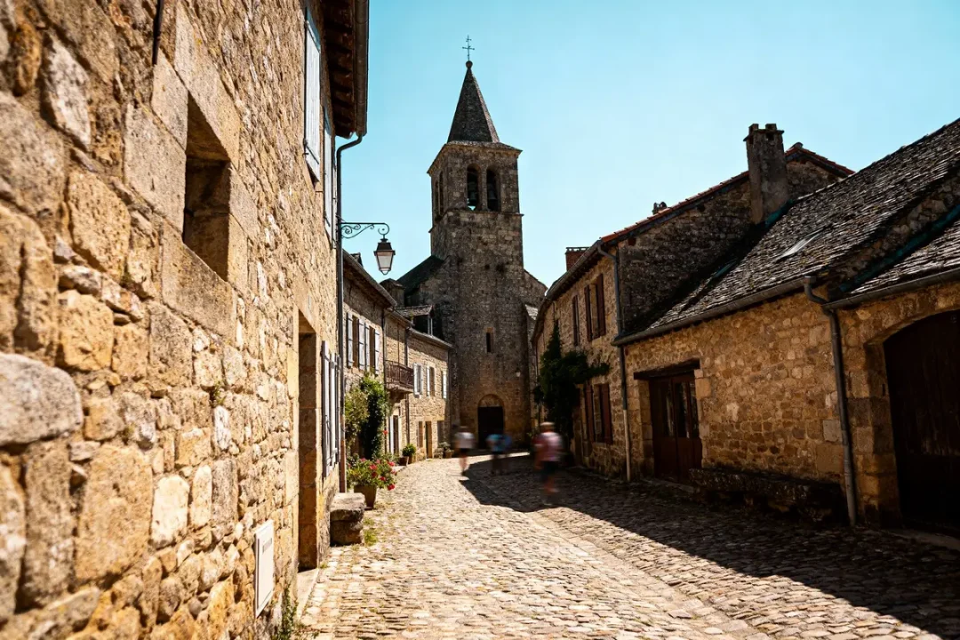 Rue pavée bordée de maisons en pierre avec église au fond, sous ciel bleu.