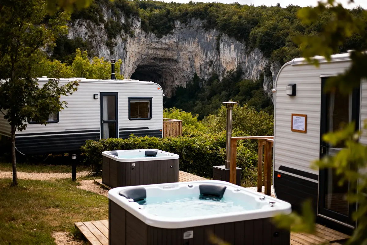 Mobil-homes avec jacuzzis devant falaise boisée, ambiance naturelle et relaxante.