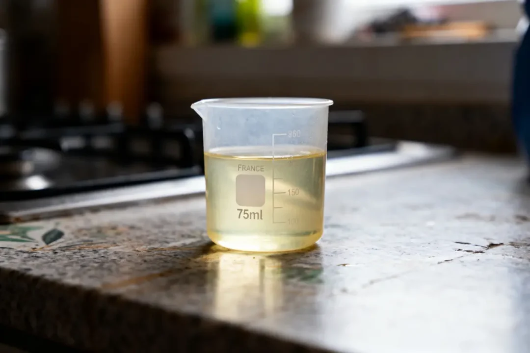 Becher transparent contenant 75 ml de liquide jaune, posé sur un comptoir de cuisine en pierre.