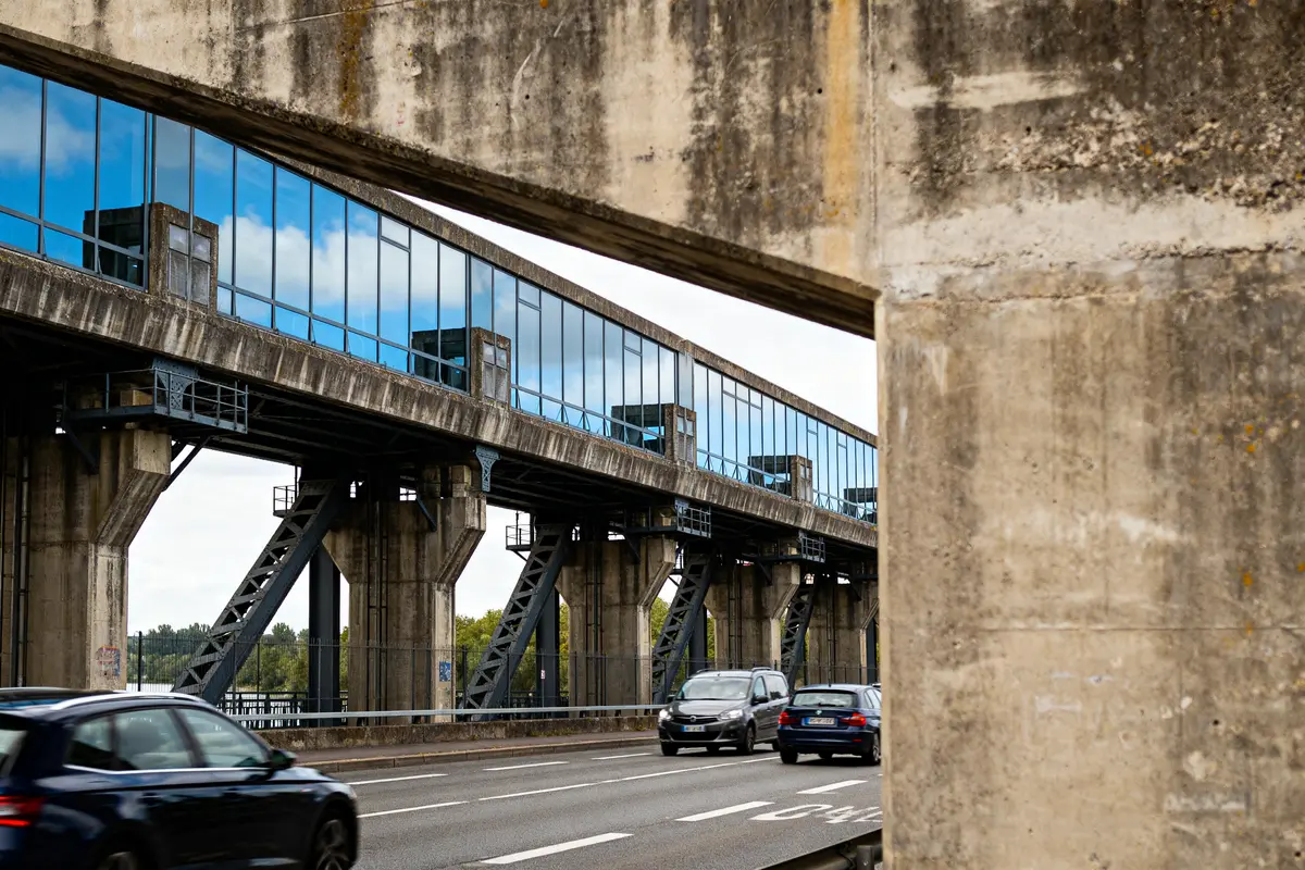 Pont en béton au-dessus route fréquentée véhicules, reflet ciel dans fenêtres, franchassis visible