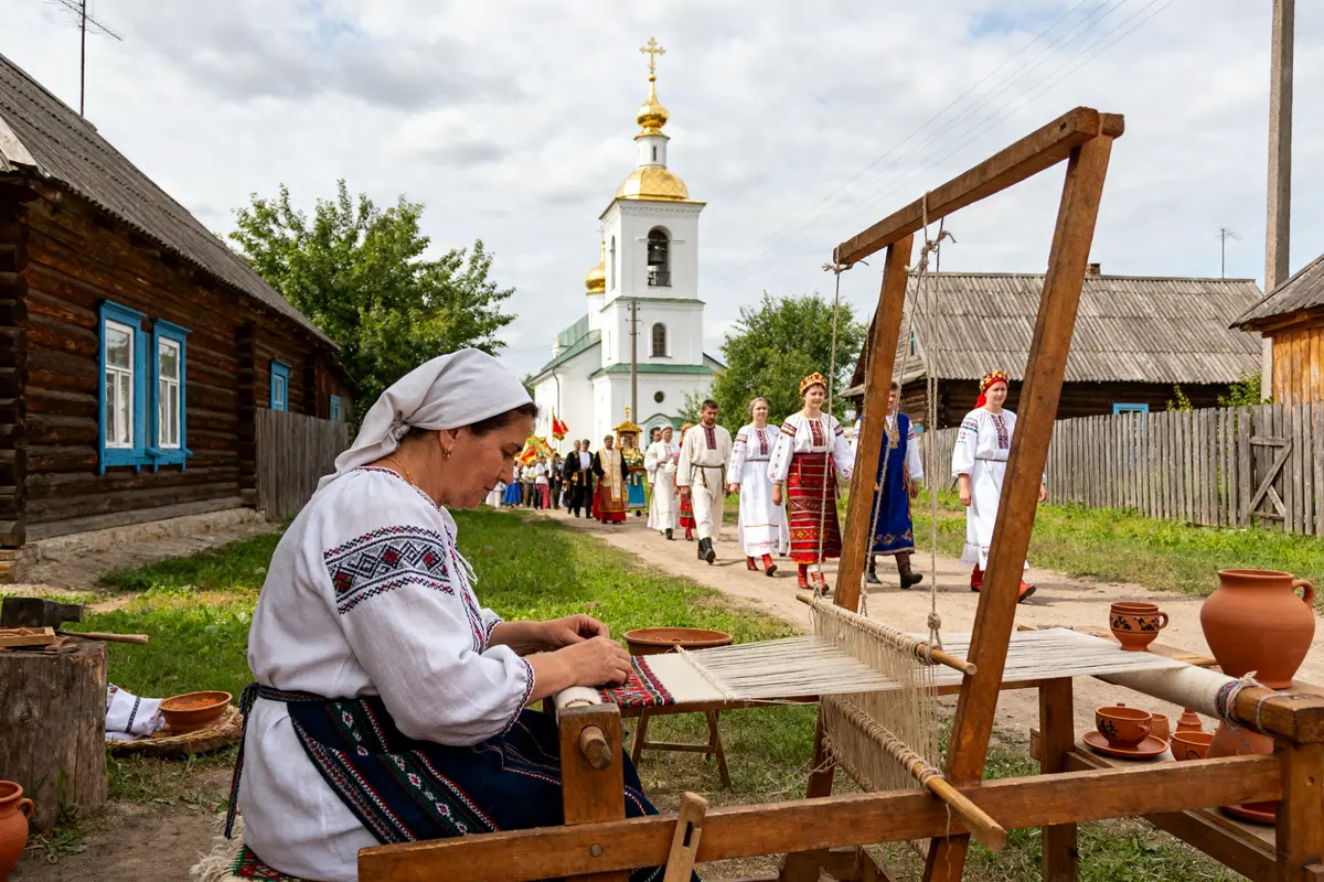 Artisan tissant près d'un village horile avec procession en tenues traditionnelles devant une église