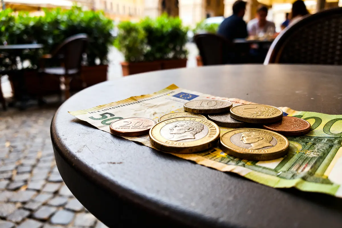Monnaies italiennes anciennes posées sur des billets euros sur une table de café extérieur