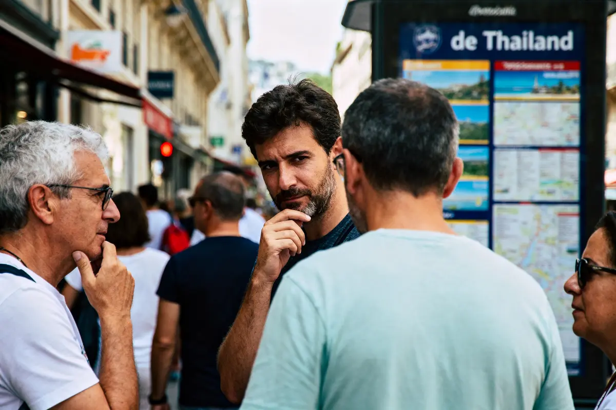 Un groupe de personnes discute en rue devant une affiche touristique thaïlandaise.