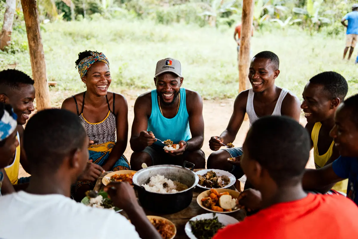 Groupe d'amis souriant partageant un repas autour d'une table à l'extérieur, ambiance joyeuse et conviviale.