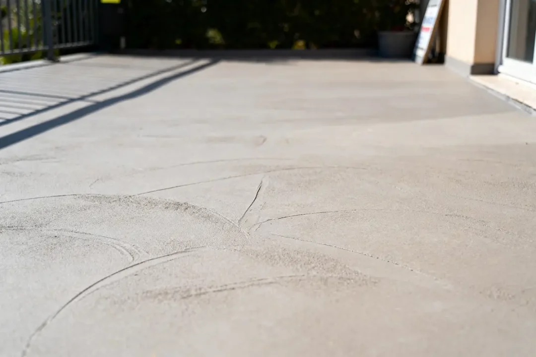 Terrasse en béton lisse avec ombre de la rambarde et pot de fleurs en arrière-plan.
