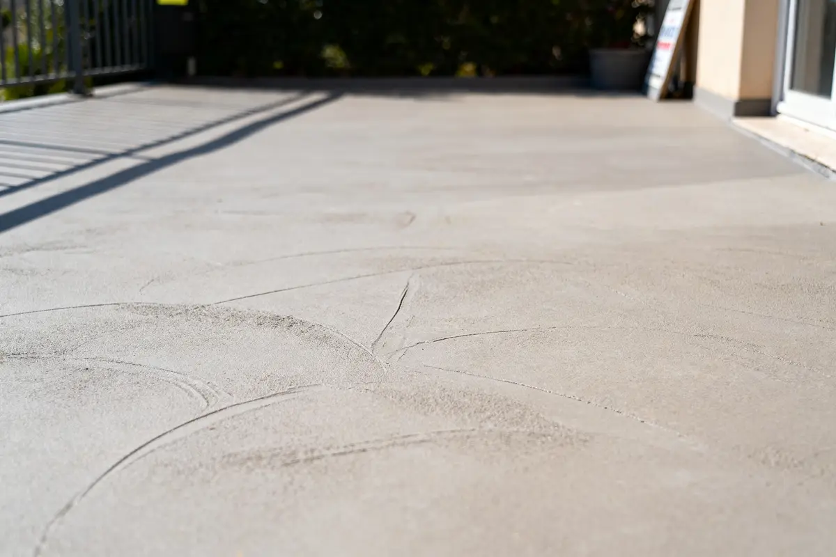Terrasse en béton lisse avec ombre de la rambarde et pot de fleurs en arrière-plan.