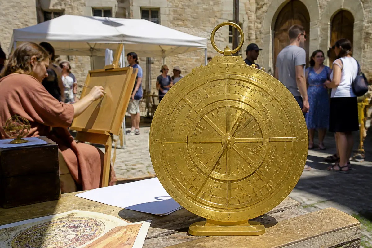 Image d'un astrolabe doré sur table, avec une femme dessinant en arrière-plan, lors d'un événement extérieur.