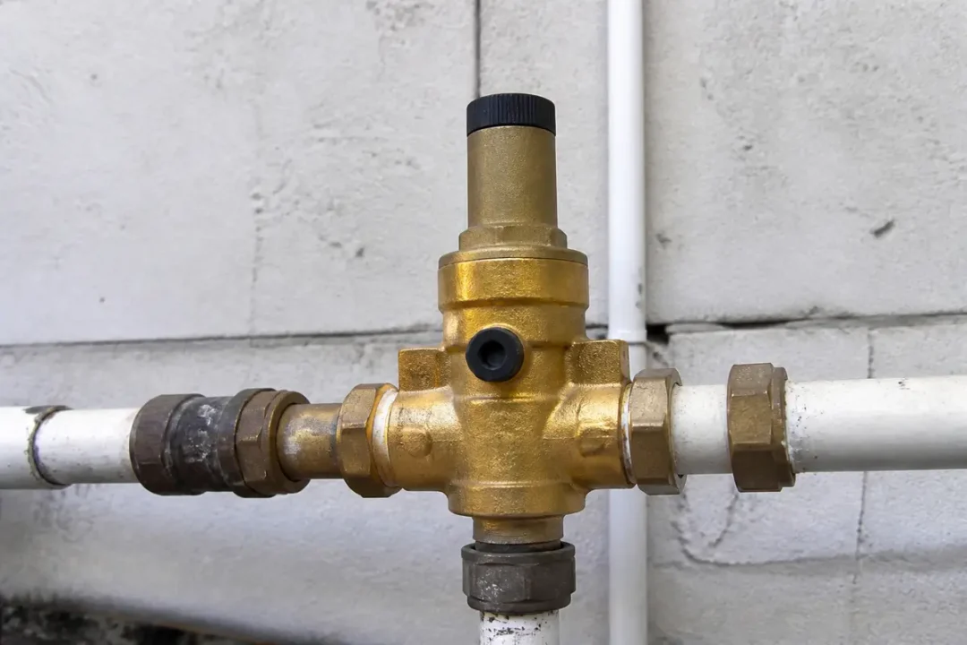 Régulateur de pression en laiton sur tuyaux blancs près d'un mur gris.