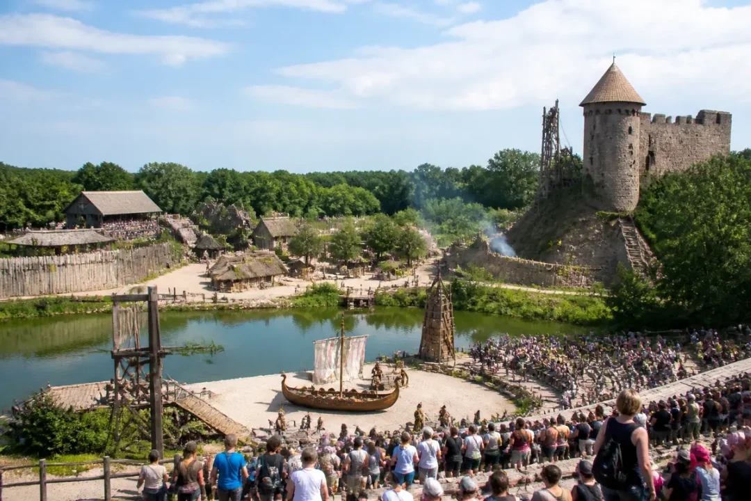 Spectacle historique en plein air au Puy du Fou, avec public et village médiéval en arrière-plan.