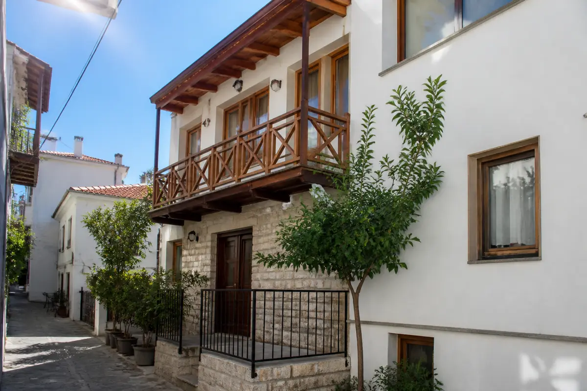 Façade de maison traditionnelle avec balcon en bois, rue étroite, arbres en pots, ciel bleu.