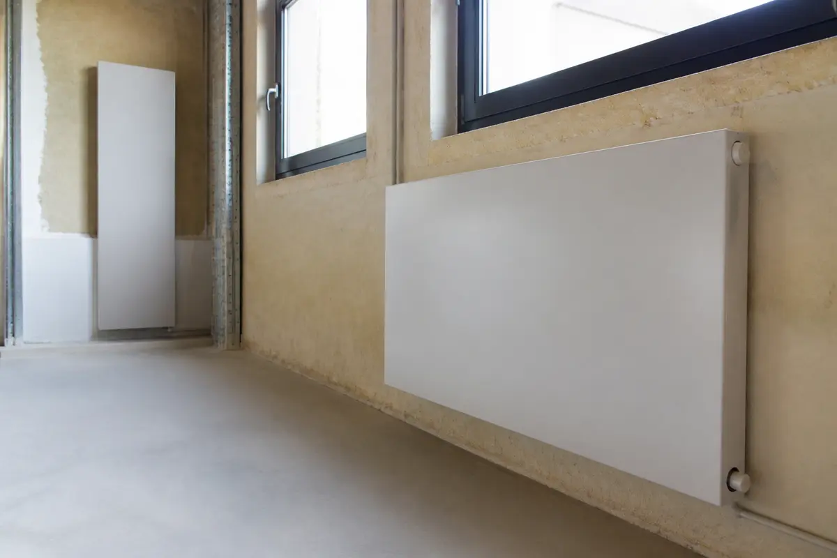 Radiateur mural moderne installé dans une pièce en rénovation avec murs isolés et fenêtres en double vitrage.