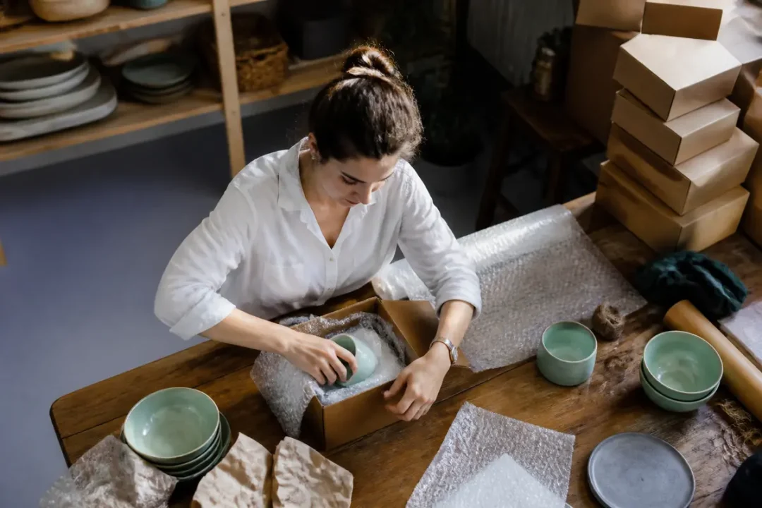 Une femme emballe délicatement une tasse en céramique dans une boîte avec du papier bulle.